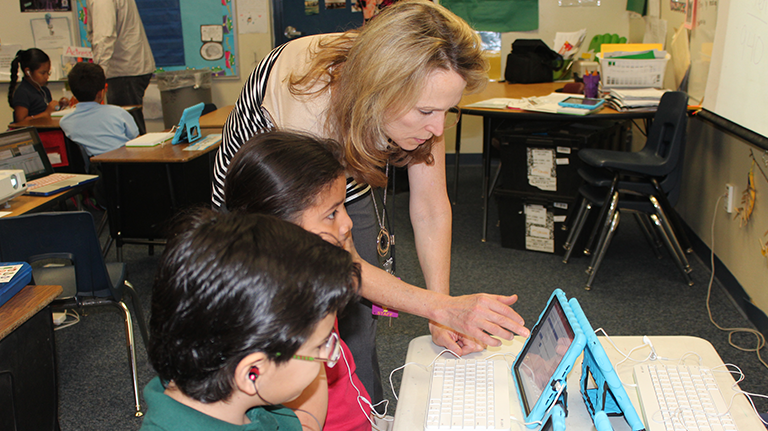Teacher showing a boy and a girl something on a blue iPad
